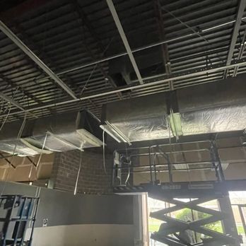 Construction site with HVAC ductwork, scissor lift, exposed ceiling, and brick wall.