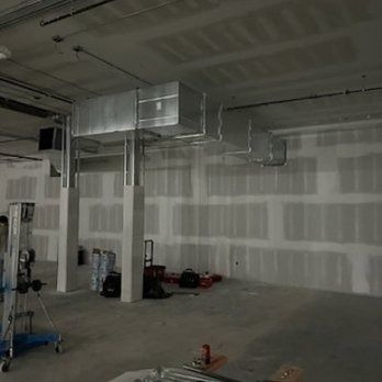 HVAC ductwork in a construction zone. Metal ducts are supported by concrete columns. Drywall walls are unfinished.