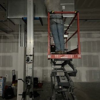 Person on a scissor lift working on ductwork inside a building with drywall.