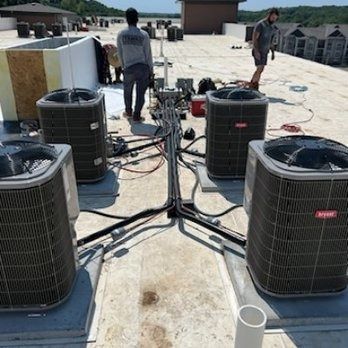 Workers install HVAC units on a flat rooftop. Black wiring connects the four units.