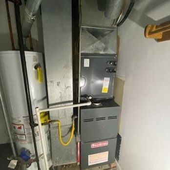 A water heater, furnace, and ductwork in a utility room. The furnace is gray, with yellow gas lines.