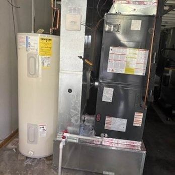 Water heater and HVAC unit in a utility room. Beige and silver appliances on concrete floor.