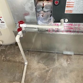 HVAC unit with white PVC drain pipes and red valves on a concrete floor.