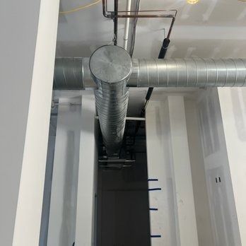 HVAC ductwork in a white-walled space; metal pipes and ductwork intersect overhead.