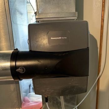 Honeywell humidifier attached to ductwork in a home. Gray unit with black section.