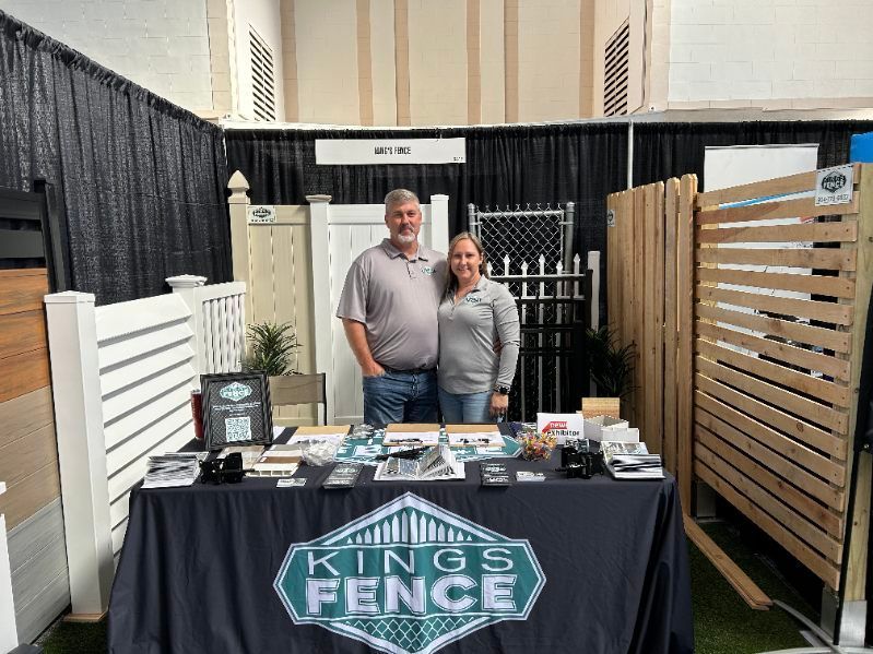 A man and a woman are standing in front of a kings fence table.