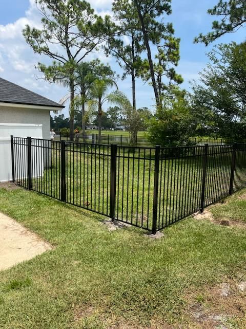 A black metal fence surrounds a lush green yard in front of a house.