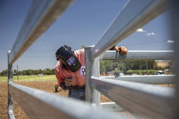 A man wearing a welding mask is working on a fence.