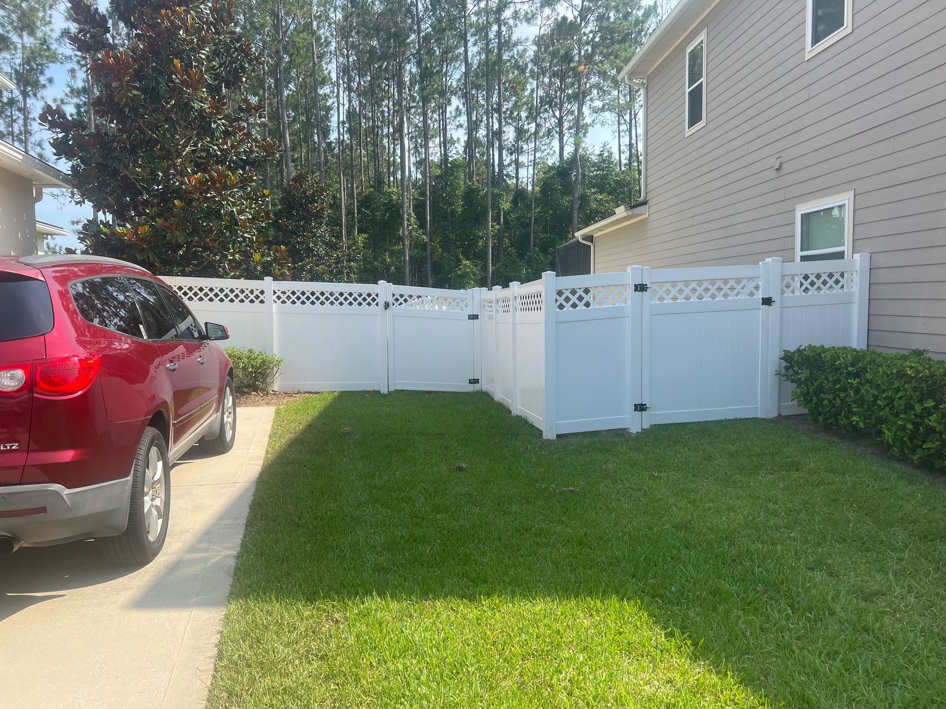 A red suv is parked in front of a white fence.