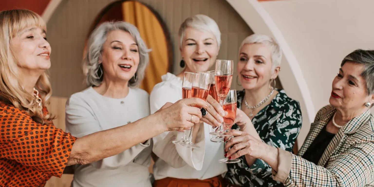 Five women toasting with champagne glasses at a cheerful indoor gathering
