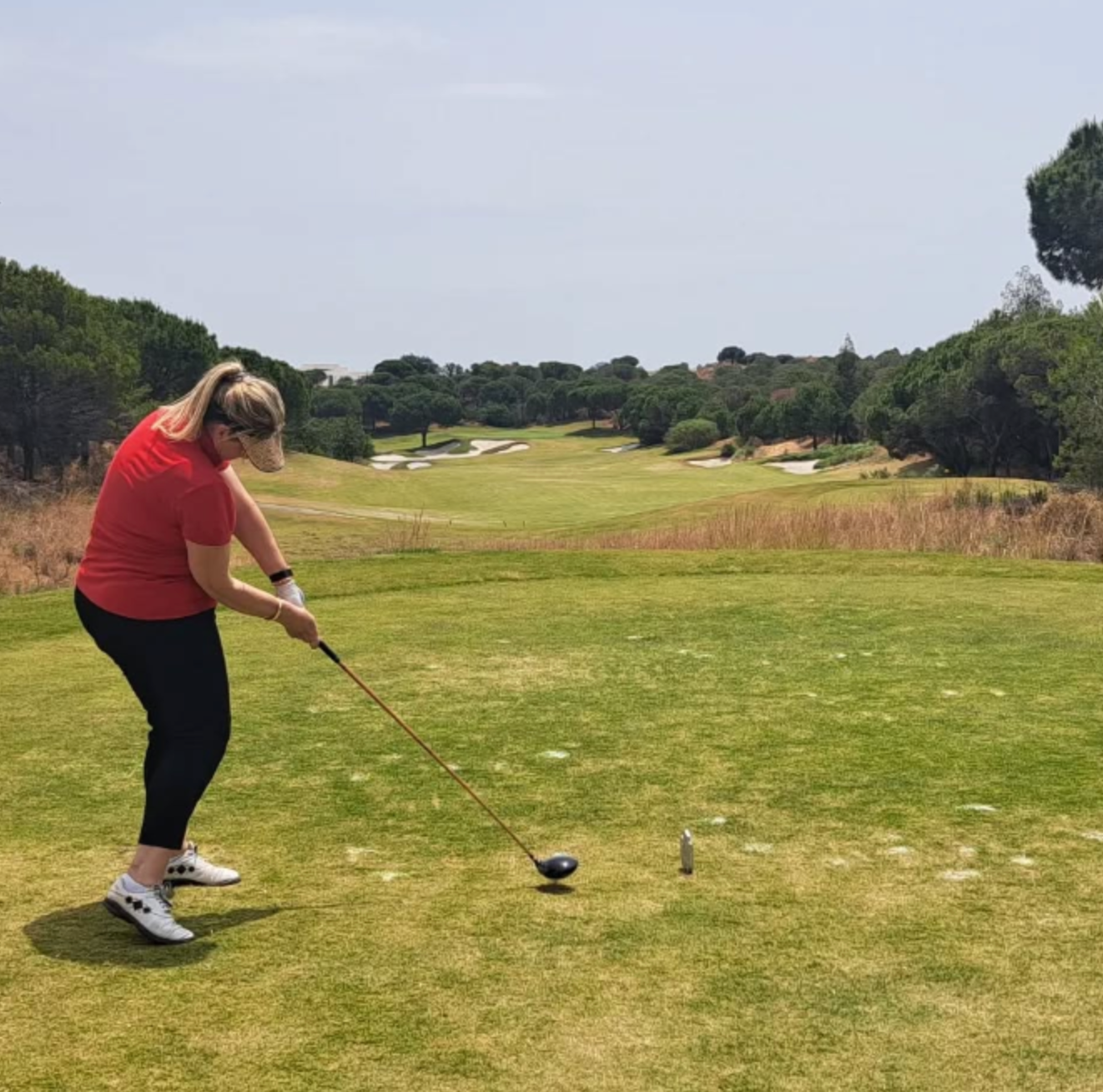 Golfer in red shirt swinging a club on a green fairway under a clear sky