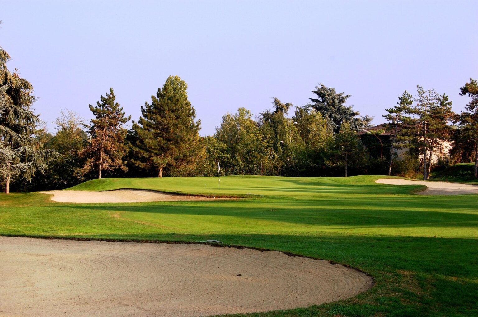 Golf course green with sand bunkers, lush grass, and trees under a clear sky