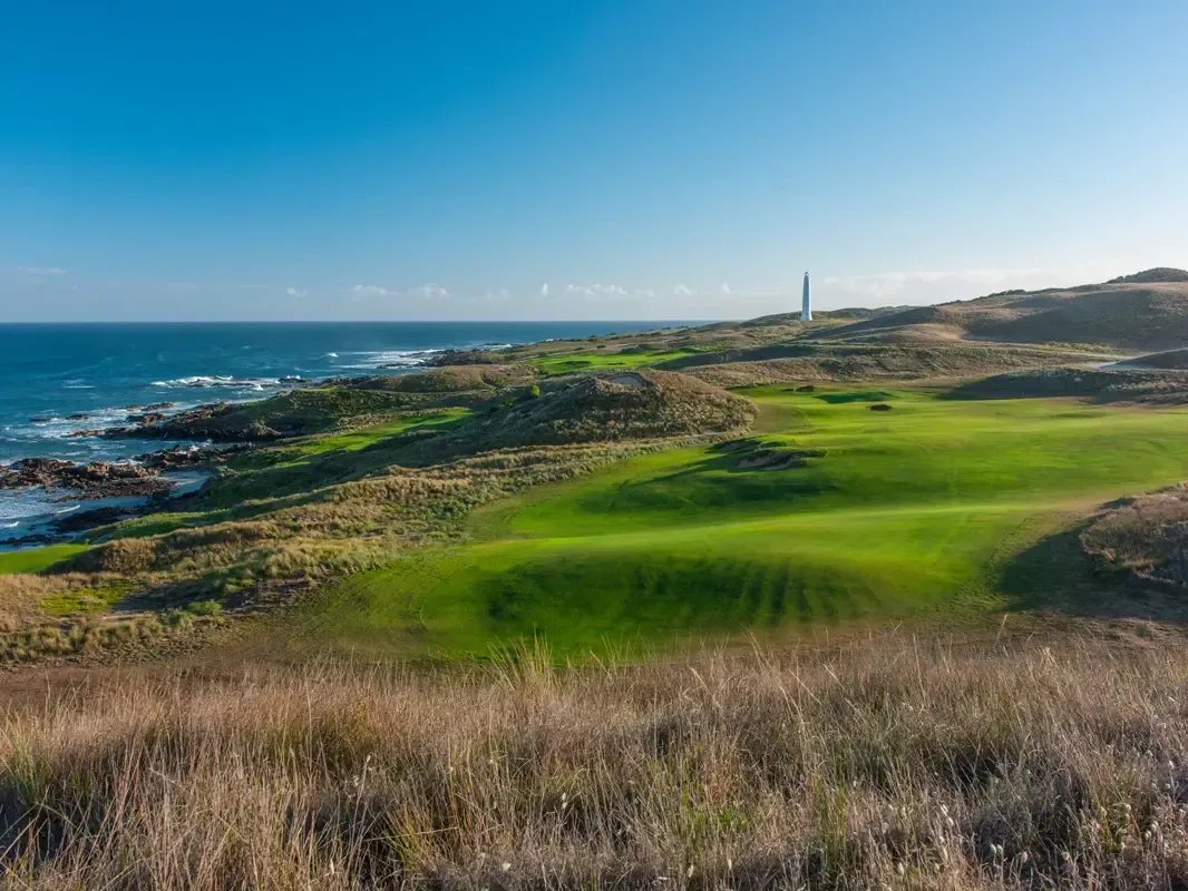 Coastal golf course with green fairways, rugged shoreline, and blue ocean under a clear sky