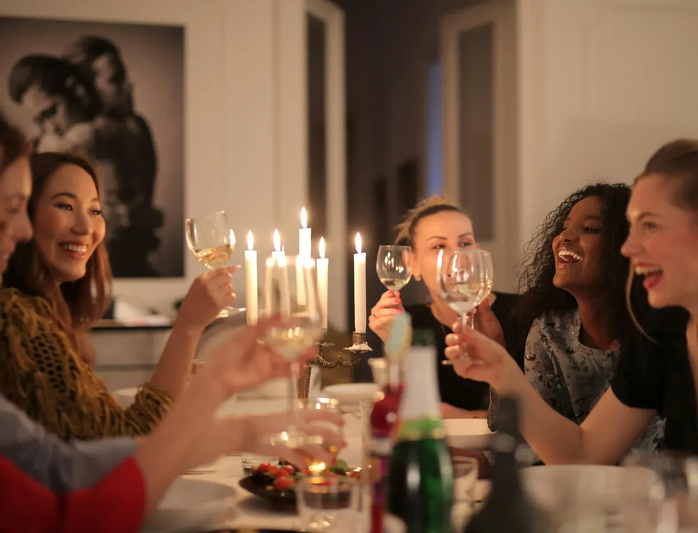 People toasting with wine glasses around a candlelit dinner table in a cozy room