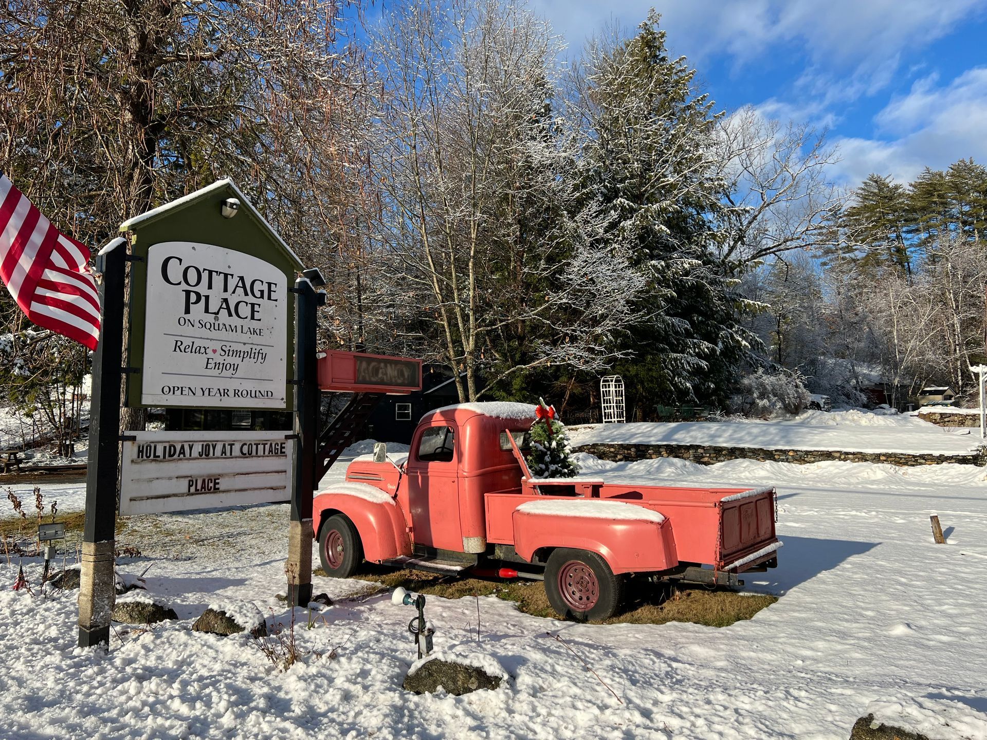 A red truck is parked in front of a sign in the snow.