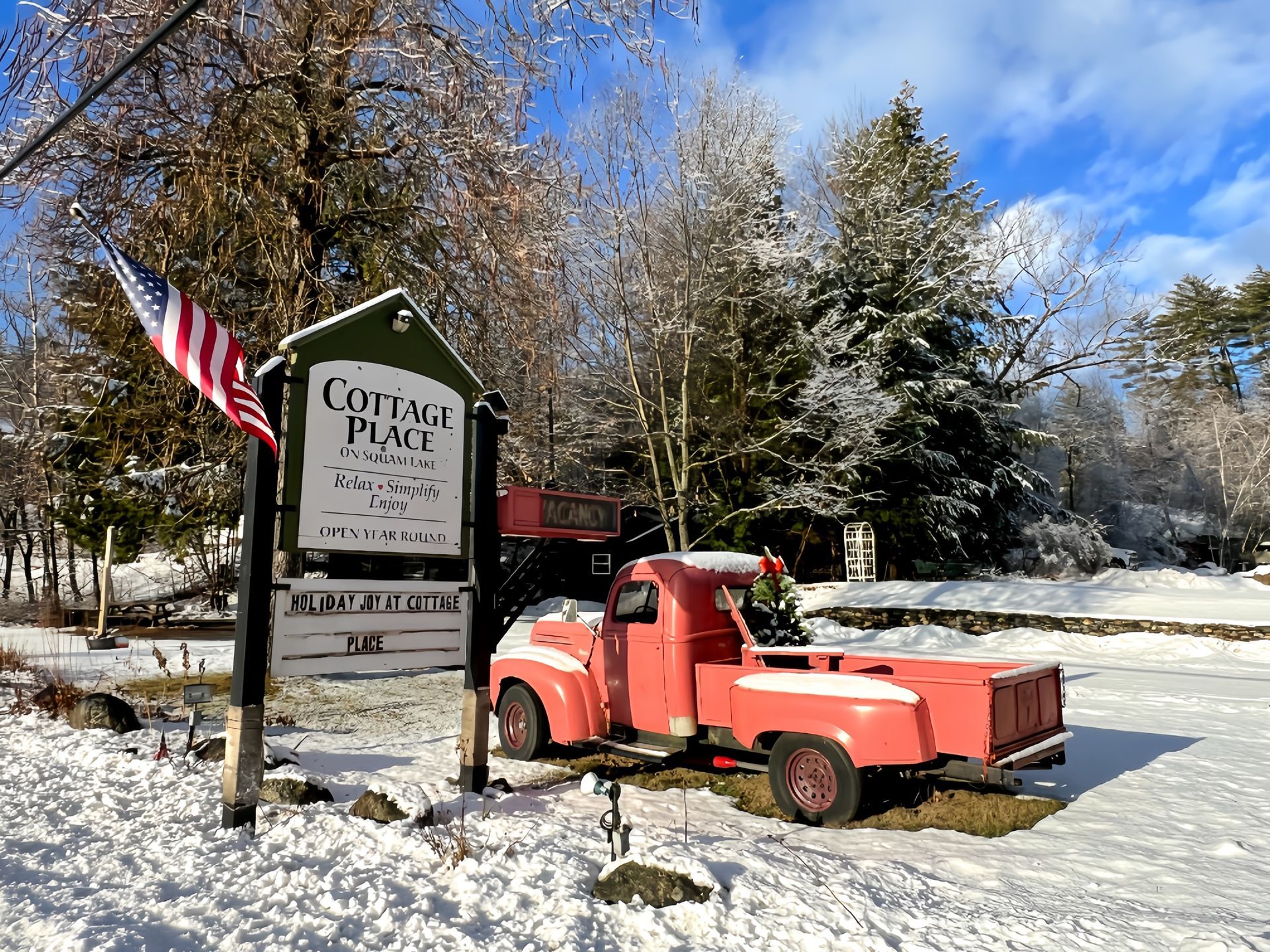 A red truck is parked in front of a sign in the snow.