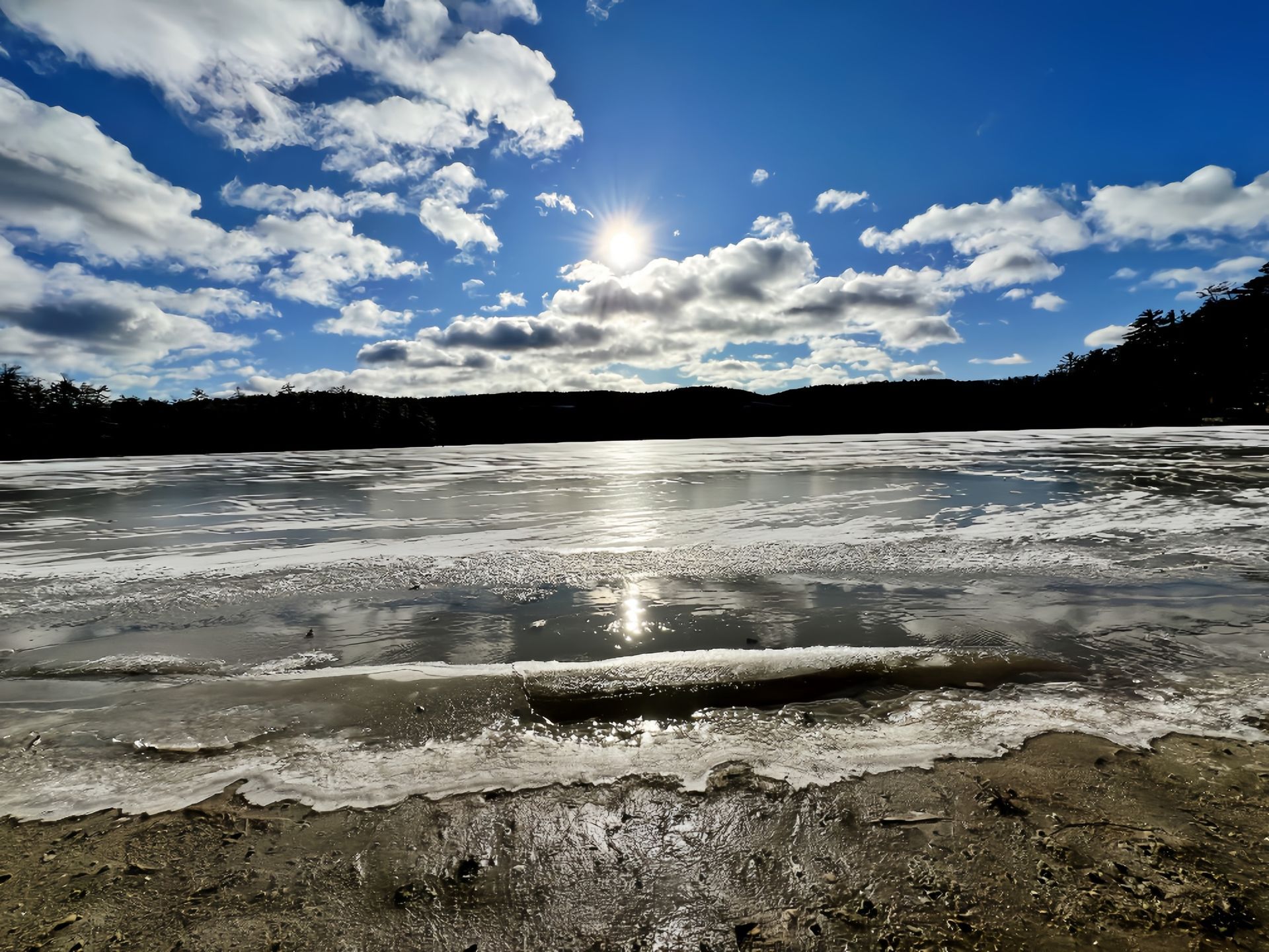 A frozen lake with the sun shining through the clouds