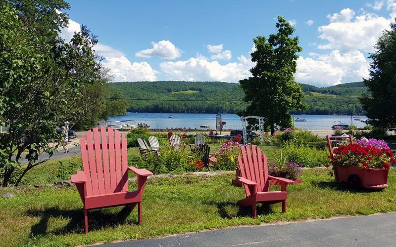 Three red adirondack chairs are sitting in a grassy area with a lake in the background.