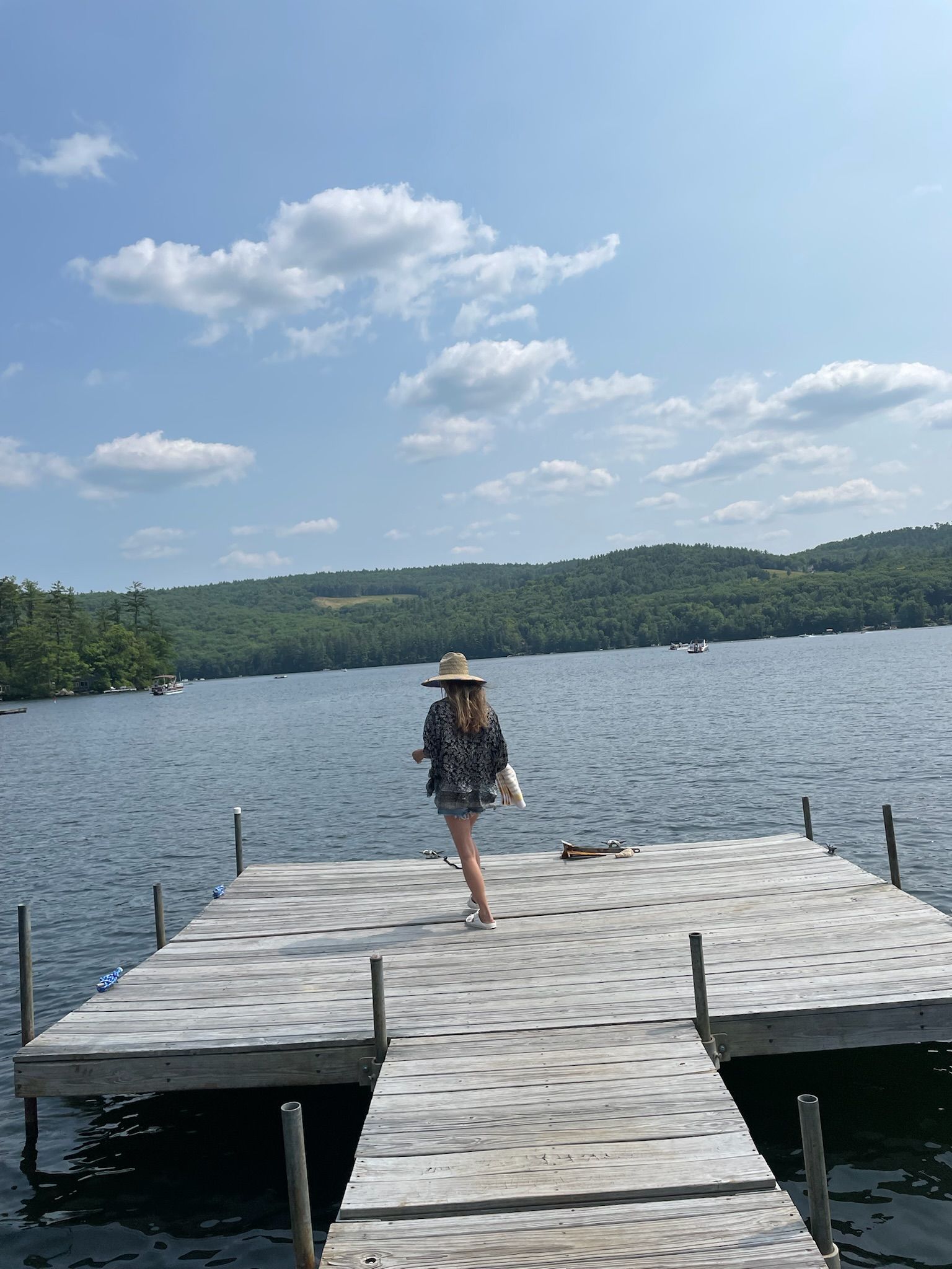 A woman is standing on a wooden dock overlooking a lake.