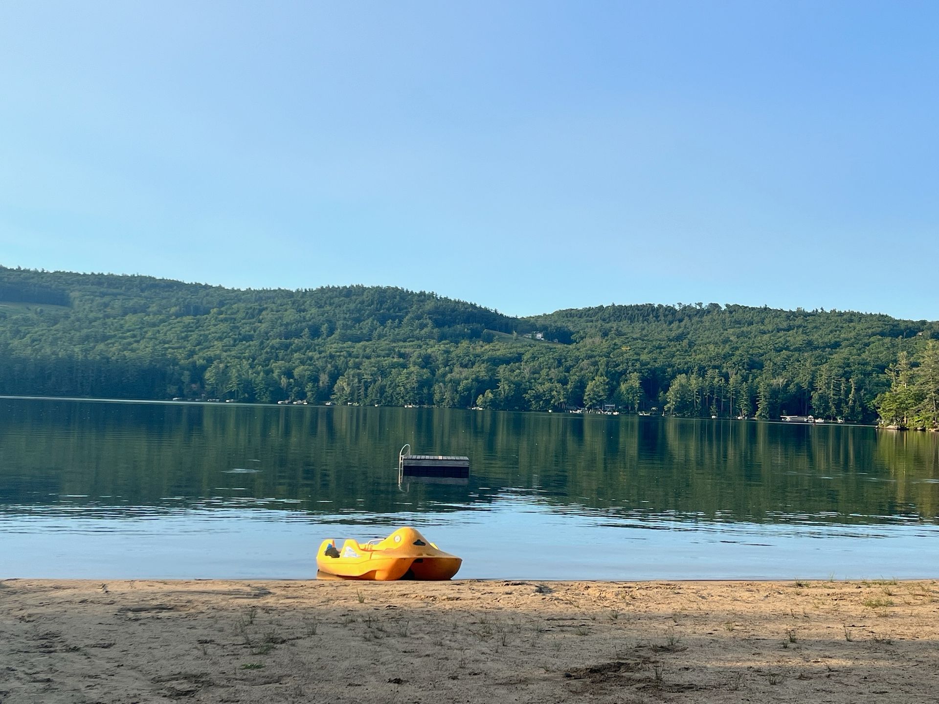 A yellow kayak is on the beach near a lake