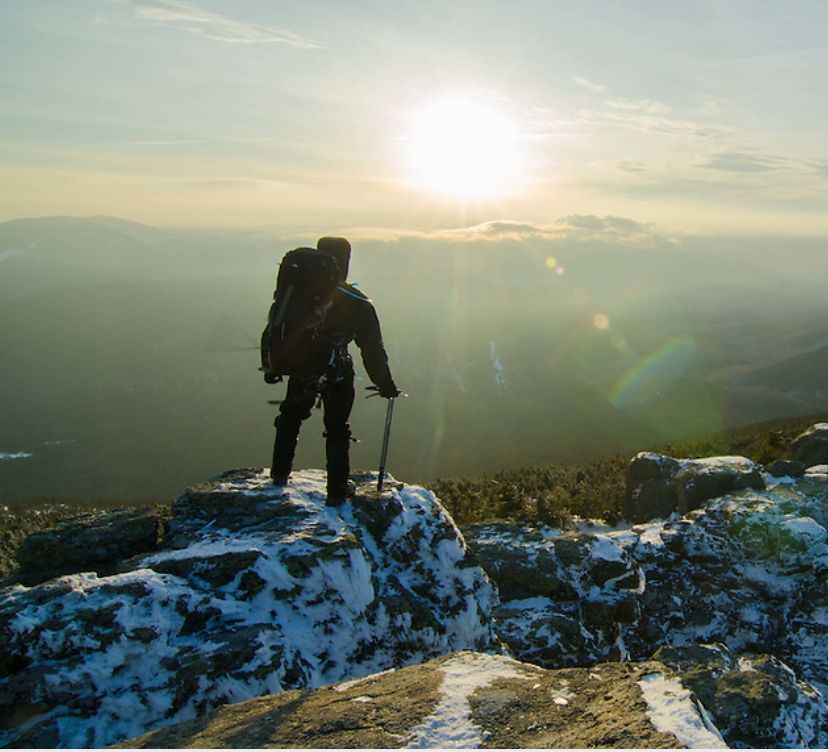 A man with a backpack is standing on top of a snow covered mountain.
