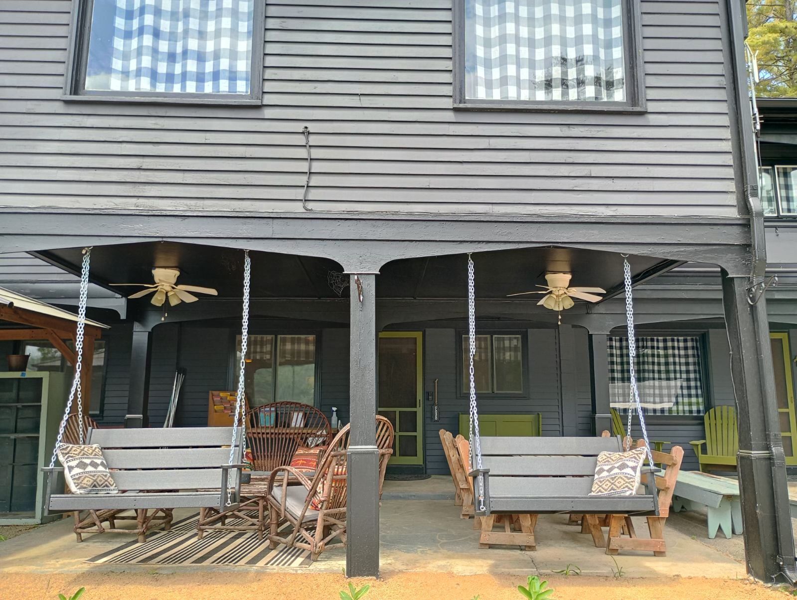 A black house with a porch with swings and a ceiling fan.