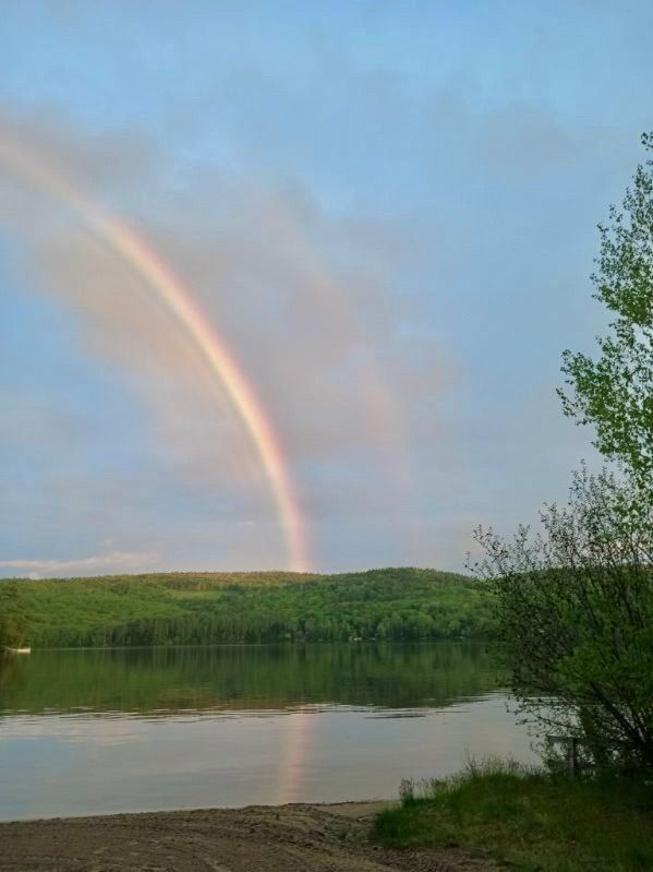 There is a rainbow over a lake in the sky.