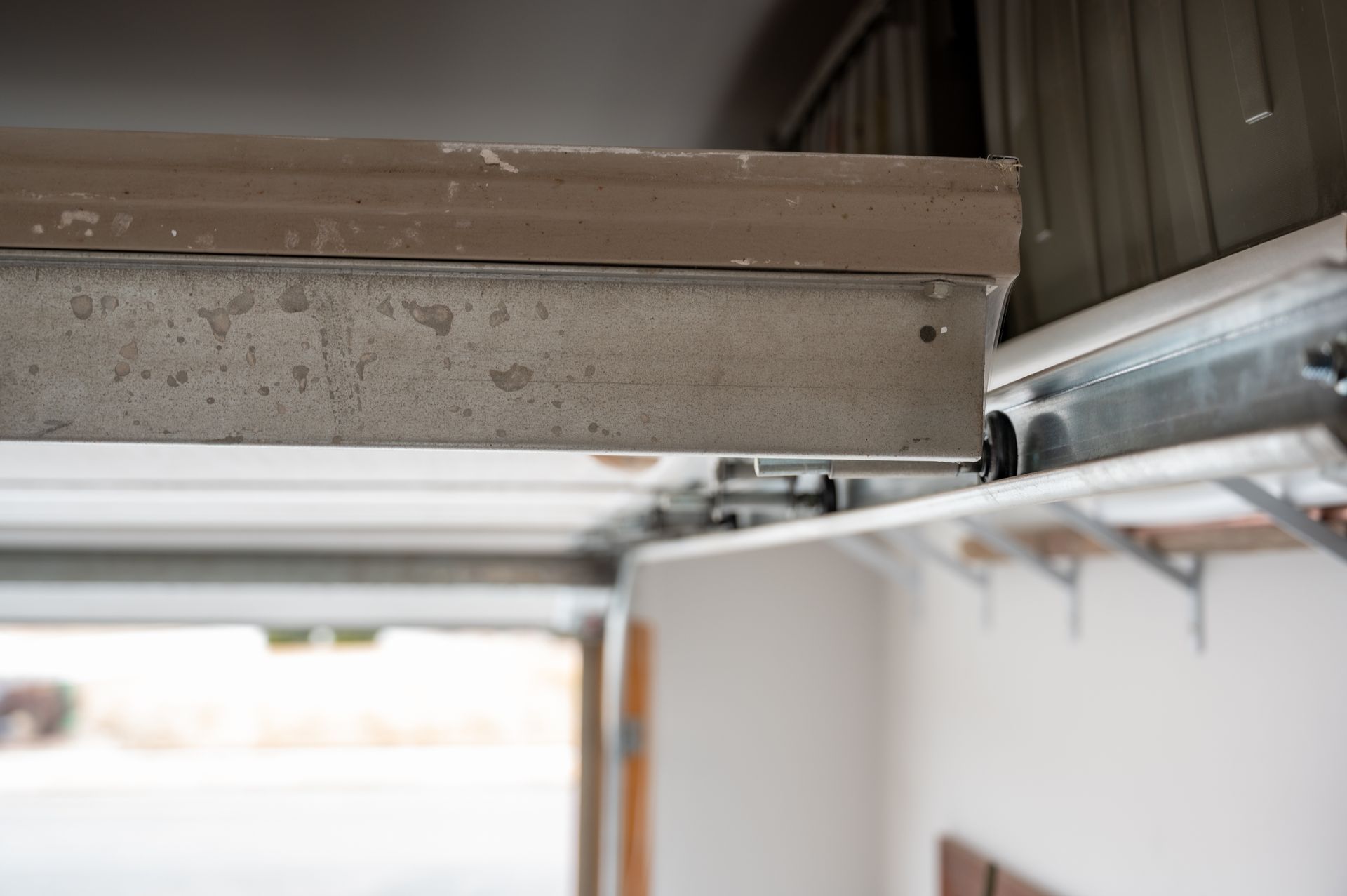 Close-up of a garage door track and overhead opener mechanism with metal rails and ceiling beams.
