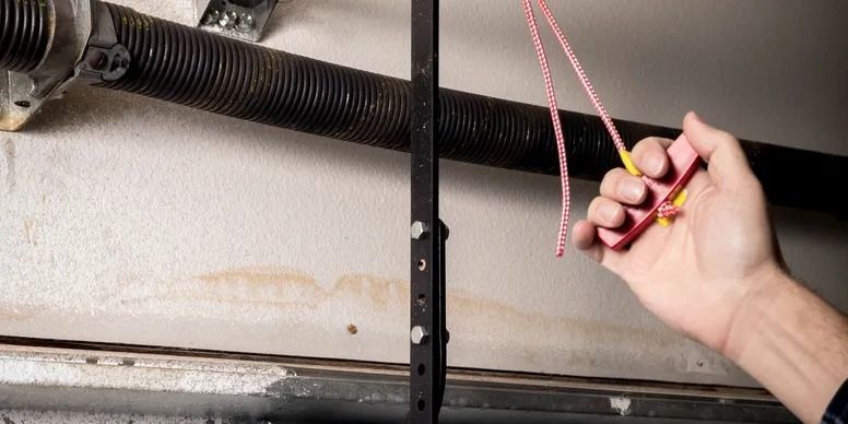 Hand holding a yellow flashlight and red cord near a garage door spring mechanism