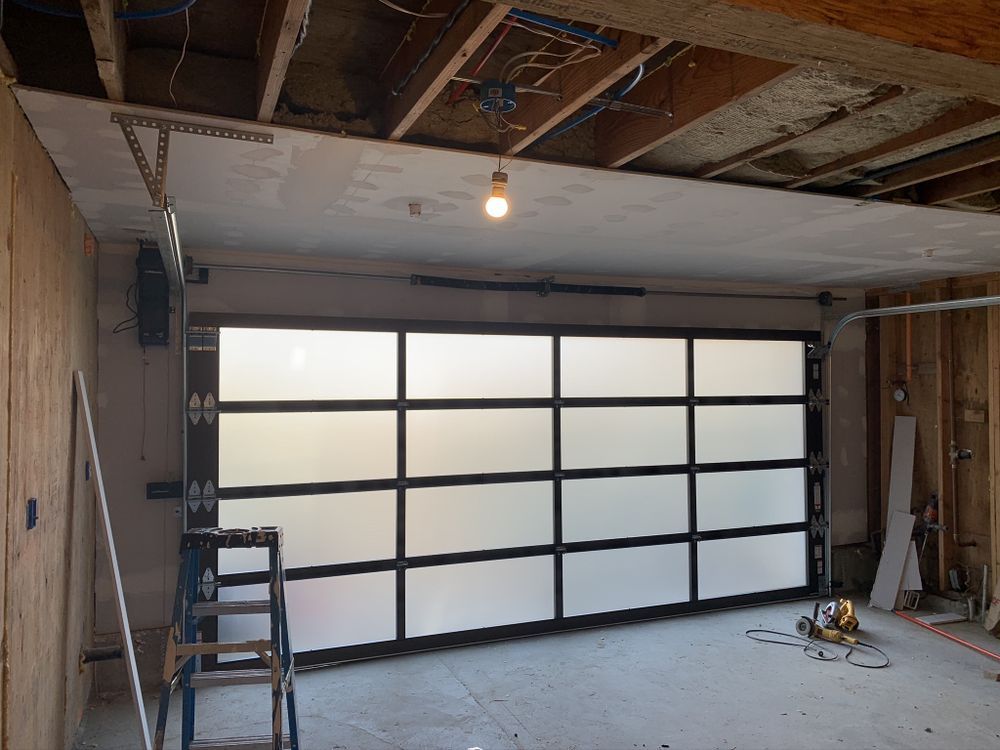 Partially finished garage with frosted glass garage door, exposed studs, and a ladder on the left