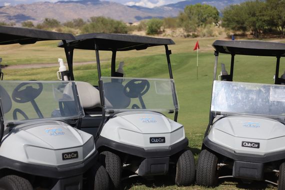 Three white golf carts parked on a golf course with a green, flag, and mountains in the background.