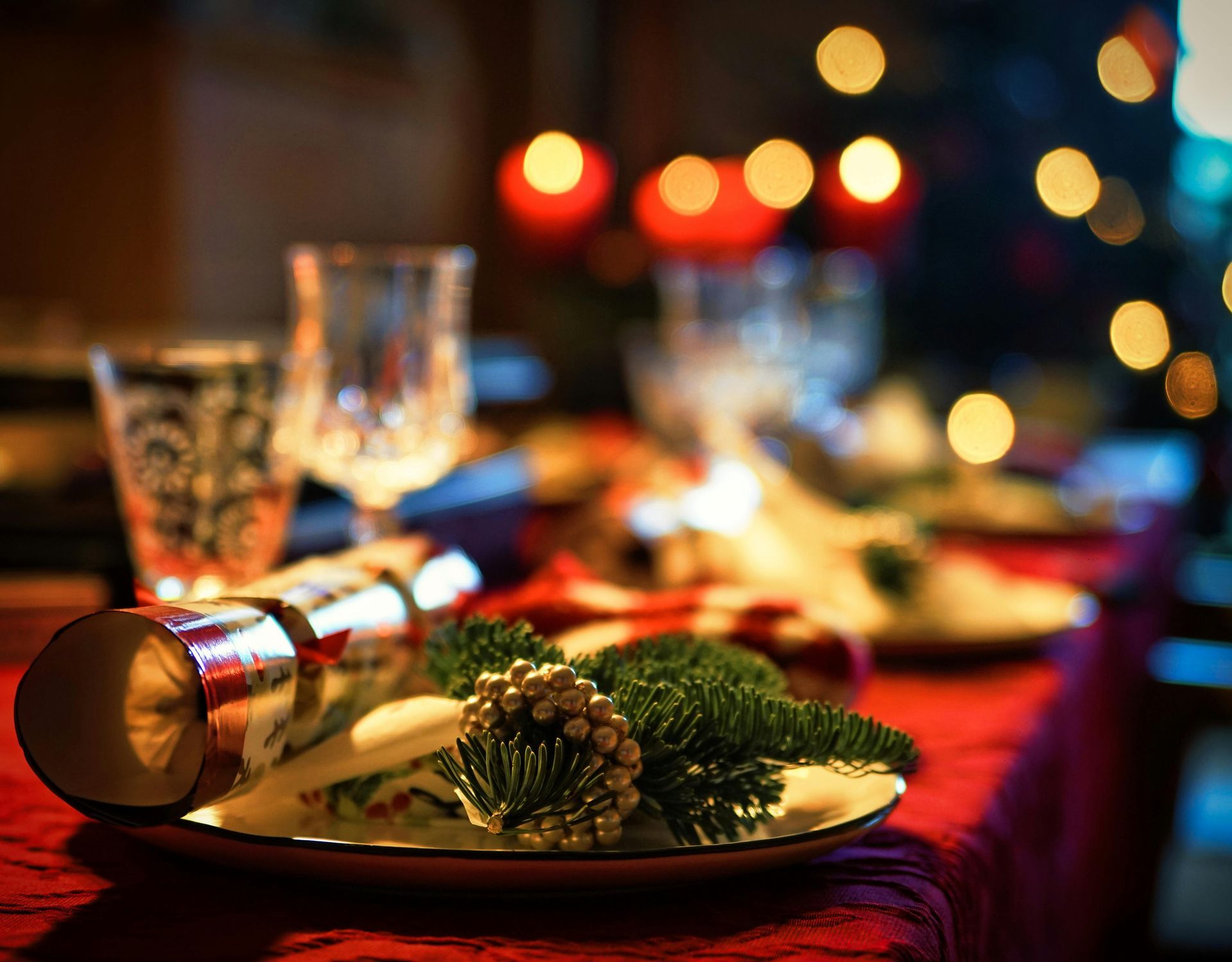 Christmas table setting with cracker, greenery, and candles.
