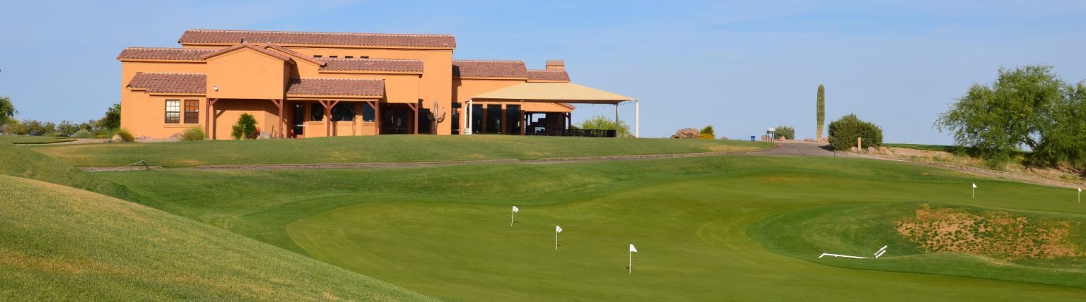 A golf course with a building in the background under a blue sky. The building is terracotta-colored.