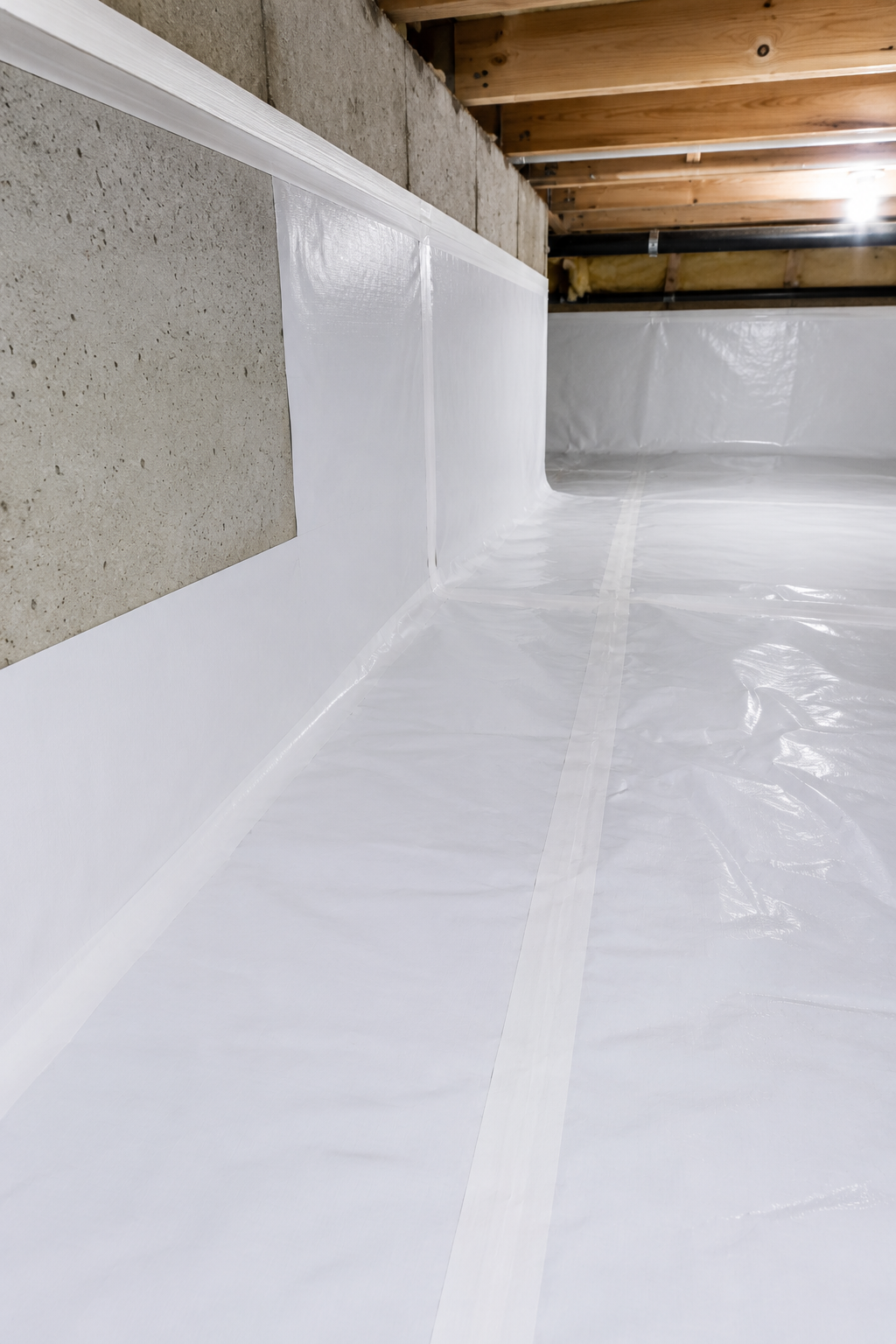 White vapor barrier lining a crawlspace under exposed wooden floor joists