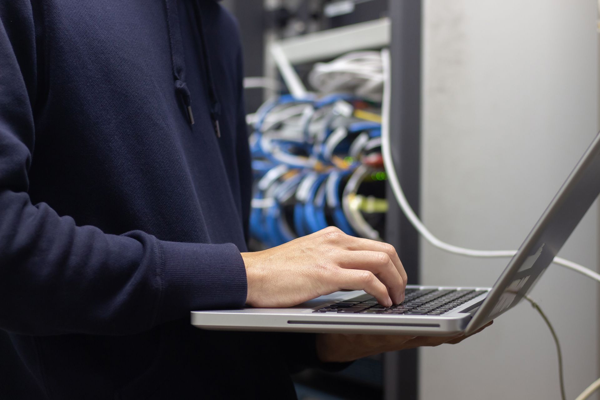 A Person is Typing on a Laptop Computer in a Server Room