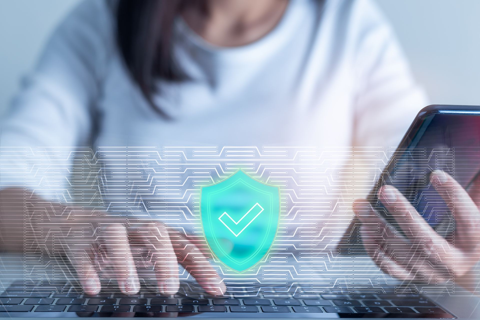 A Woman is Typing on a Laptop and Holding a Cell Phone