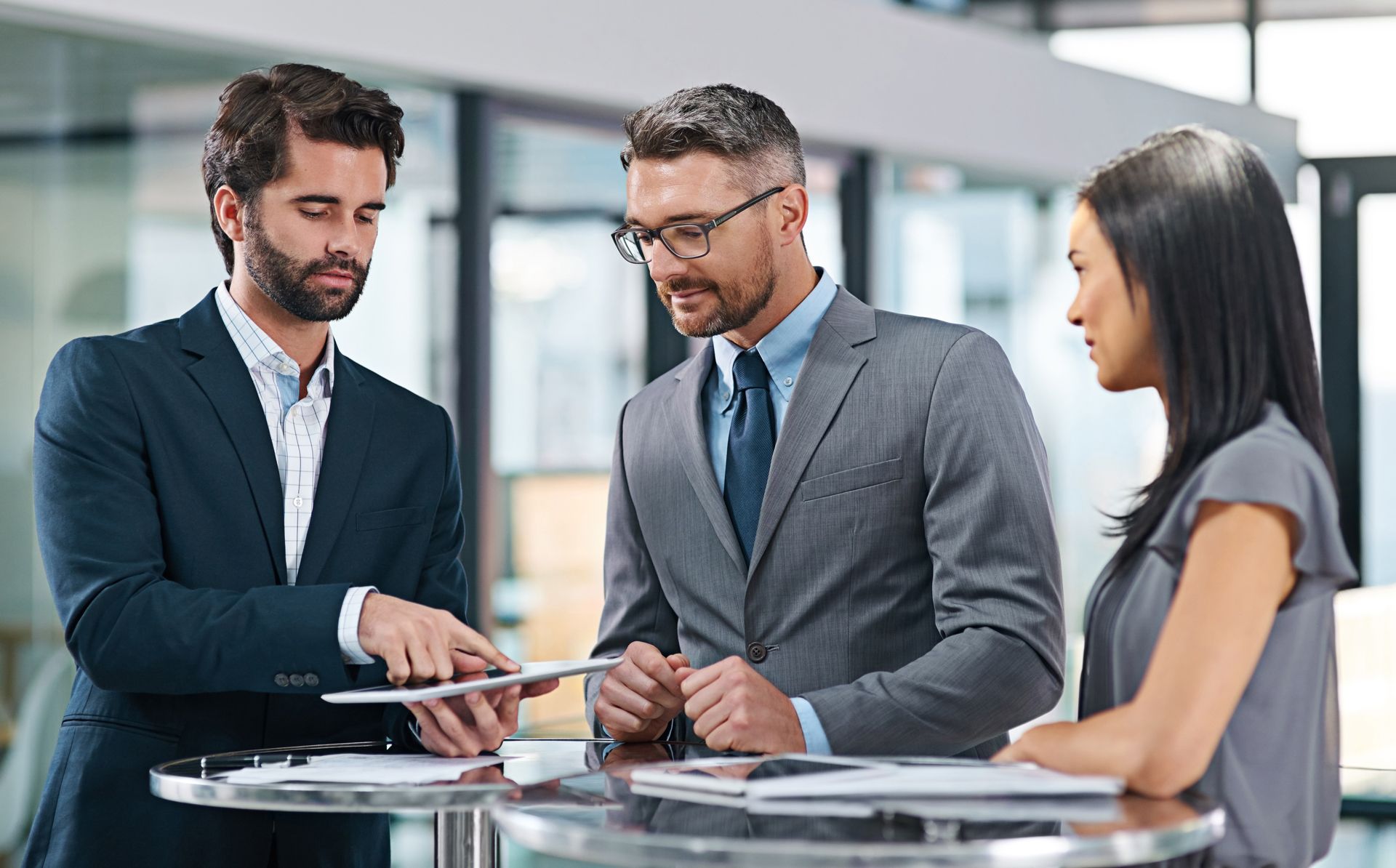 A Group of Business People Are Standing Around a Table Looking at a Tablet