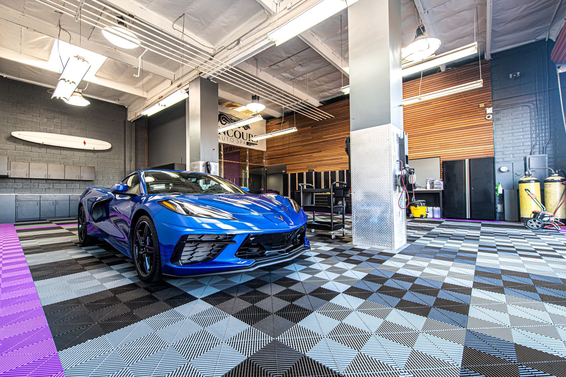 Blue sports car parked in a modern garage with checkerboard flooring and bright lighting.