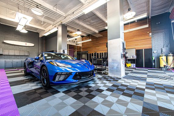 Blue sports car parked in a modern garage with checkerboard flooring and bright lighting.