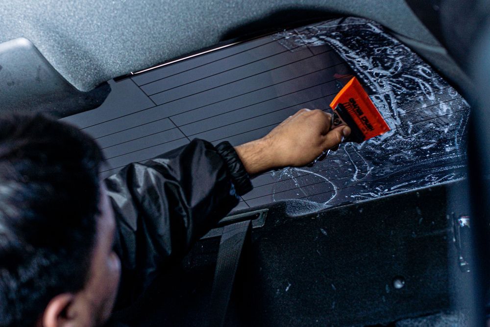A man is cleaning the back window of a car with a squeegee.