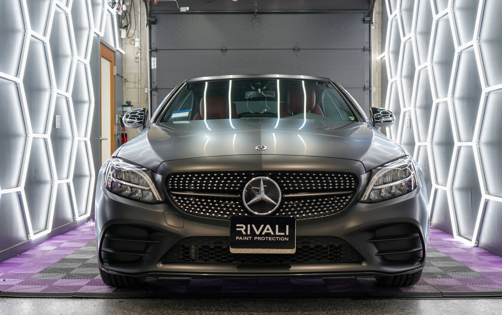 A gray Mercedes-Benz car, inside a detailing bay with honeycomb lighting.