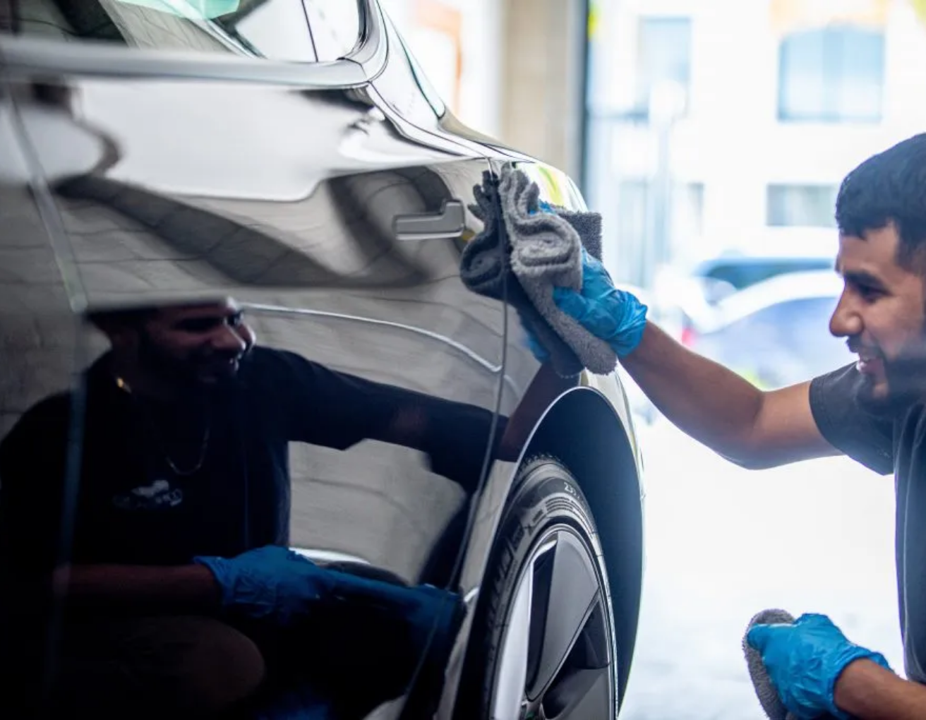 A man is cleaning a car with a cloth in a garage.