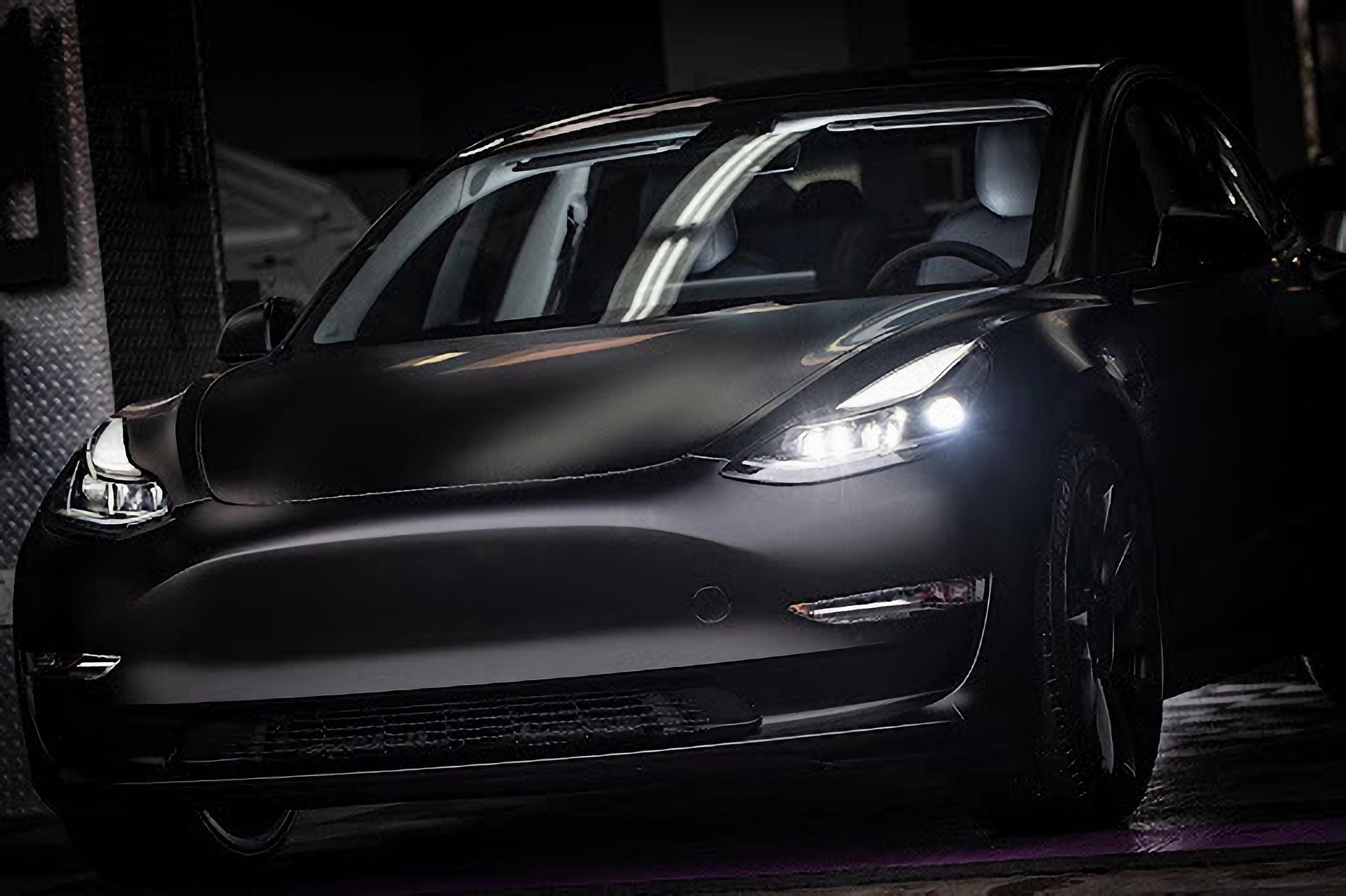 A black tesla model 3 is parked in a dark parking lot.