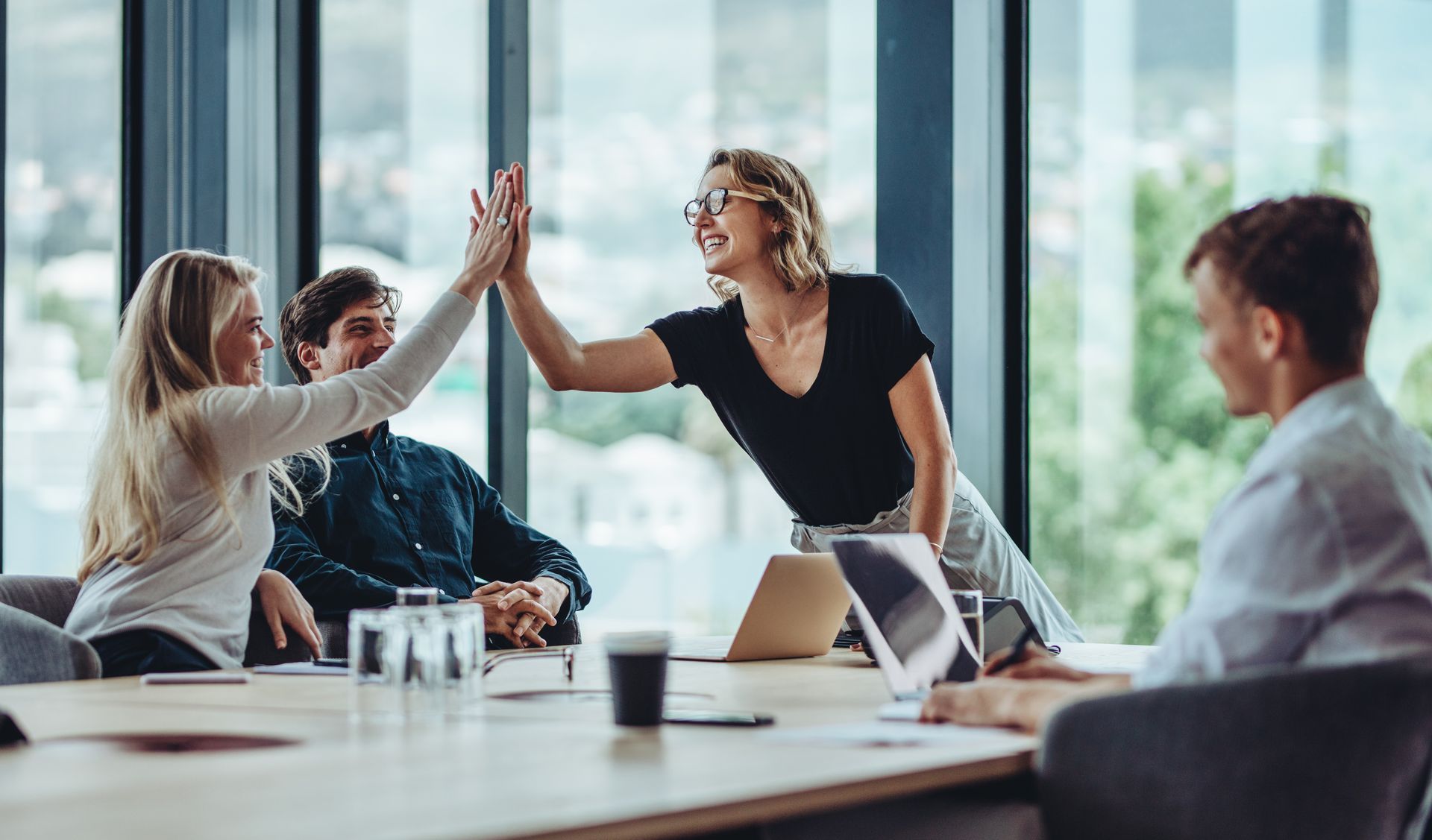 A diverse group of colleagues high-fiving during a bright office meeting.