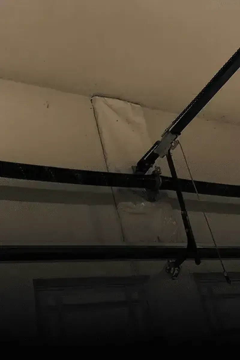 A white mounting plate attached to a garage wall, securing the metal track of an overhead garage door opener.