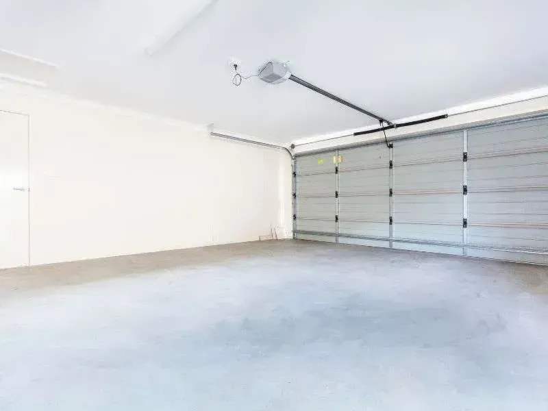 A bright, empty garage with white walls, a gray concrete floor, and a closed sectional metal garage door.