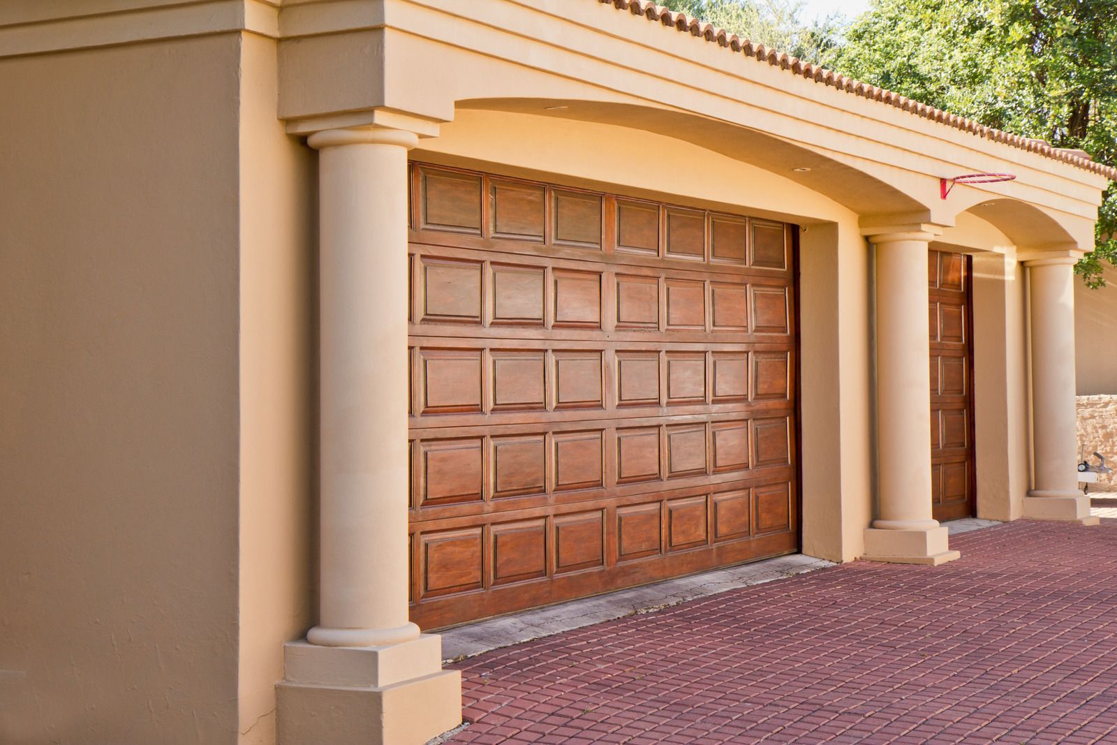 Beige stucco house with a large brown wooden garage door and brick driveway