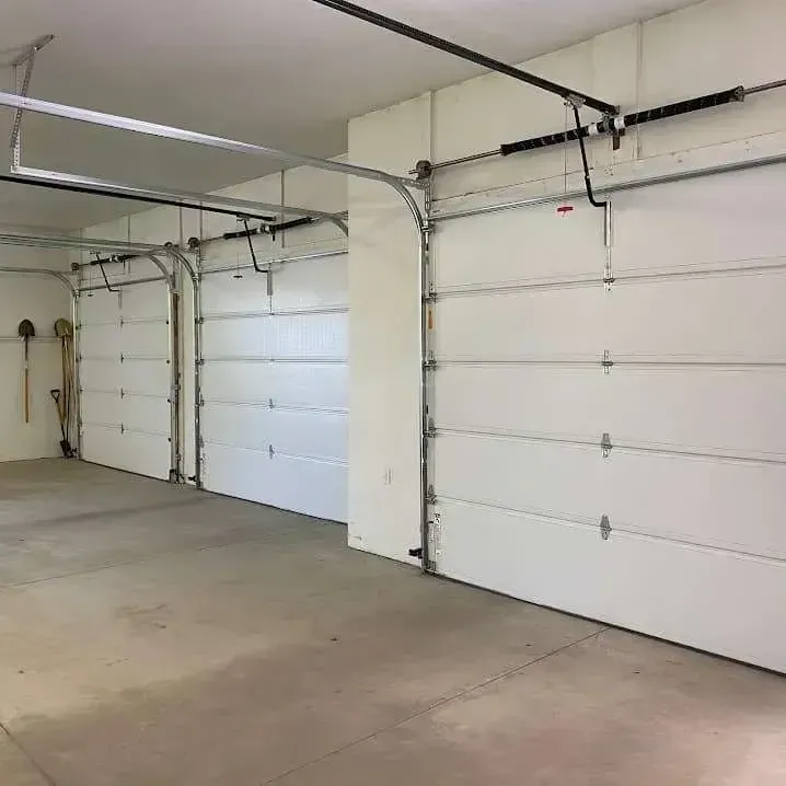 Three white garage doors side-by-side in a clean, empty concrete garage.