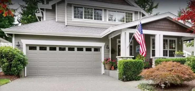 A gray two-story house with a white garage door, front porch, and an American flag hanging by the entrance.