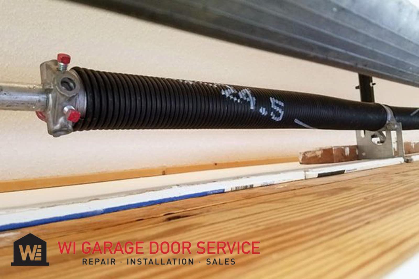 Garage door torsion spring installed above wooden garage door with WI Garage Door Service watermark